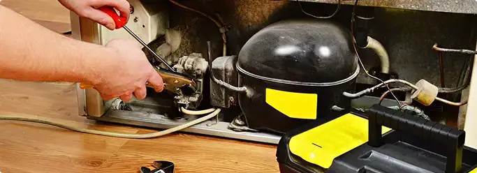 Refrigerator repair technician fixing the compressor and wiring in Dayton, KY