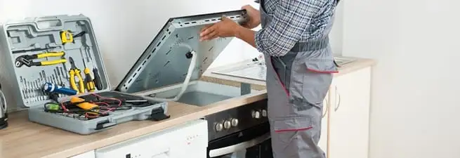 Cooktop repair technician lifting a built-in stovetop for service in Cincinnati, OH