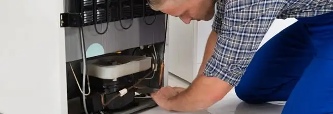 Refrigerator repair technician servicing the compressor and condenser area in Cincinnati, OH