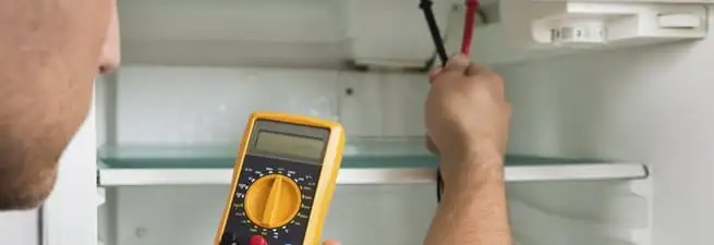 Refrigerator repair technician testing electrical components with a multimeter in Cincinnati, OH