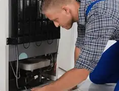 Refrigerator repair technician servicing the compressor and condenser area in Cincinnati, OH